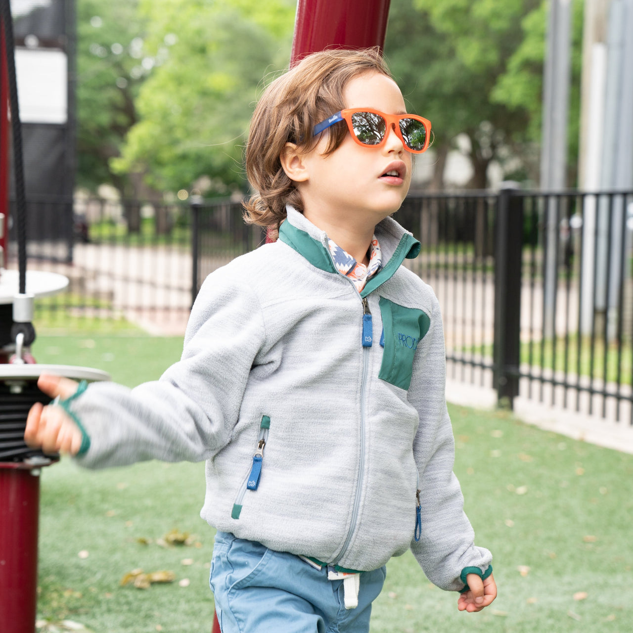 Little boy wearing an orange and blue polarized kids sunglass with reflective lenses and 100% UVA/UVB protection.