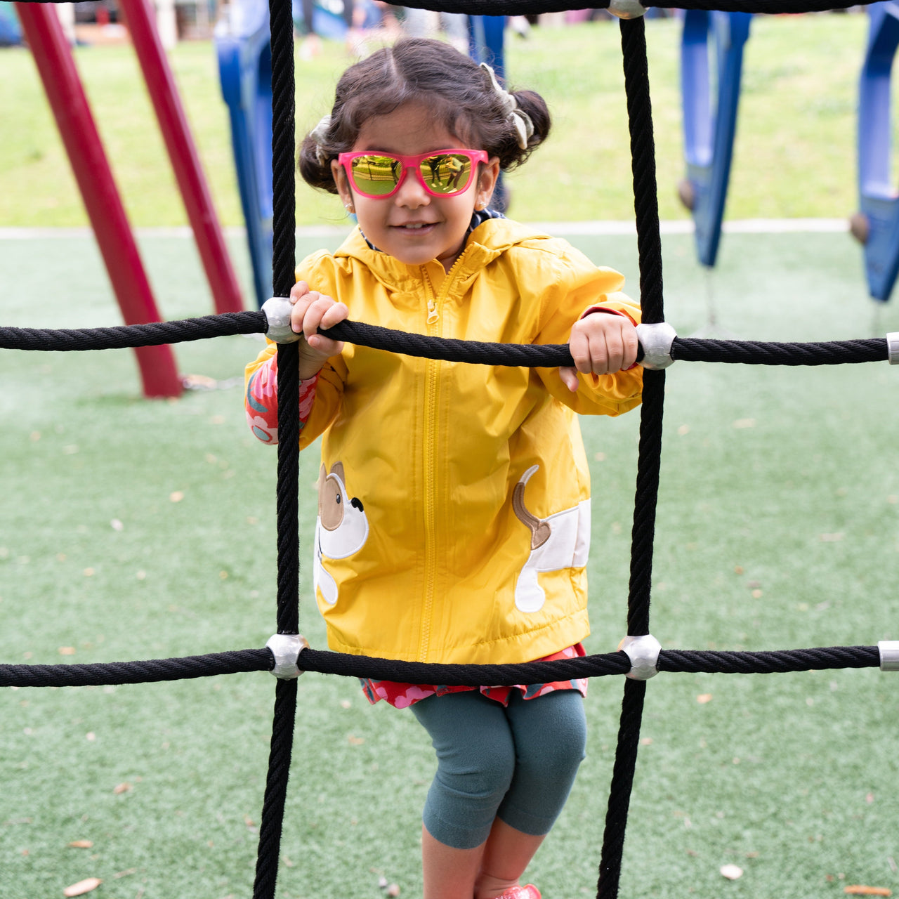 Little girl playing on a playground wearing sunnies littles pink polarized kids sunglasses.